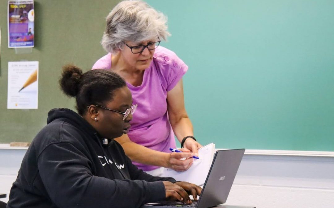 An old woman helping a younger woman with something on a laptop
